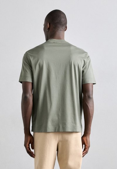 T-shirt a maniche corte verde oliva, realizzato in morbido cotone, con una vestibilità rilassata e colletto girocollo, con cuciture visibili lungo l'orlo.