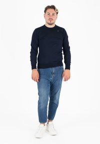 Morsko modra rebrasta dolga majica, v kombinaciji s svetlo modrimi ožjimi kavbojkami in belimi supergami. Na prsih je subtilen znak.