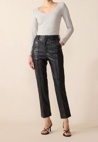 Haut gris à manches longues associé à un pantalon noir en cuir taille haute avec des coutures frontales et une coupe slim, porté avec des talons noirs à brides.