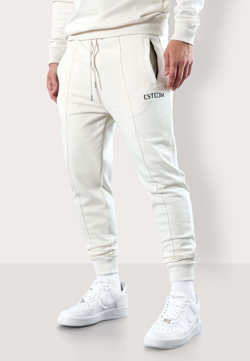 Joggers en coton blanc à coupe slim, dotés de poches latérales et d'un logo noir brodé. Associés à des baskets blanches et à des poignets côtelés.