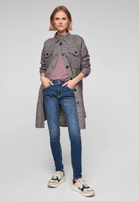 Šedá kostičkovaná dlouhá košile s dvěma předními kapsami přes mauve top, spárovaná s modrými skinny džíny a vícebarevnými teniskami.