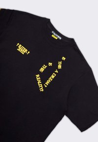 T-shirt nera in cotone con testo giallo: "IUTER 2002" e "È QUESTO UN SOGNO?" con vestibilità rilassata e collo rotondo.