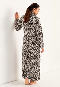 Lång, lätt, djurmönstrad morgonrock med svarta leopardfläckar på en beige bakgrund. Har långa ärmar och en krage.
