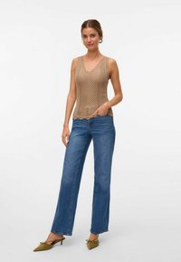 Top de punto beige sin mangas con patrón de espiga y dobladillo ondulado, combinado con pantalones vaqueros de pierna ancha azul claro y zapatos de punta verde oliva.