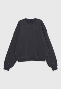 Felpa nera con maniche larghe, scollatura tonda e cuciture visibili. Presenta bottoni a pressione sui polsini e un design con vestibilità rilassata.