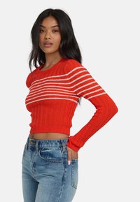 Czerwony sweter z prążkowanego materiału z białymi poziomymi paskami, okrągłym dekoltem i krótkim krojem, zestawiony z niebieskimi dżinsami z wysokim stanem.