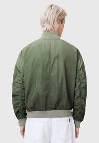 Olive green bomber jacket with gathered sleeves, ribbed cuffs, and a smooth, slightly glossy texture; designed for a relaxed fit.