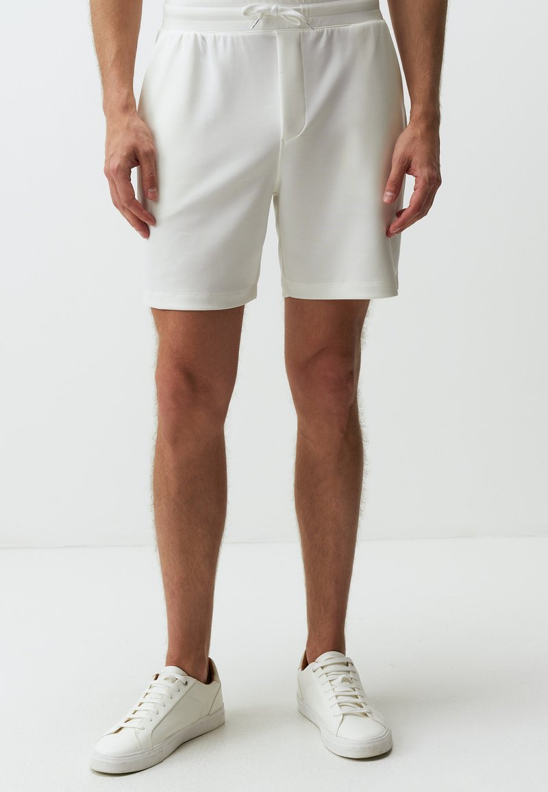 Pantaloni sportivi bianchi realizzati in tessuto liscio, dotati di una vita elasticizzata con cordino, che arrivano appena sopra il ginocchio. Indossati con sneakers bianche.
