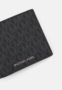 Black textured wallet with embossed design, featuring a metallic "MICHAEL KORS" logo and smooth edges.