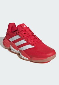 Red athletic shoe with mesh upper, white three-stripe design, padded collar, and cushioned sole for support and comfort.