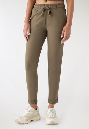 Pantaloni jogger verde oliva con vita elasticizzata e coulisse, caratterizzati da una vestibilità corta e polsini arrotolati, abbinati a sneakers di colore chiaro.