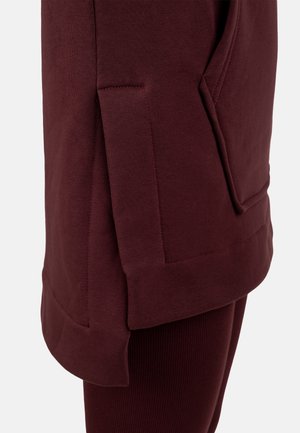 Bordowa bluza z bocznym rozcięciem i dużą przednią kieszenią. Miękka bawełniana tkanina o gładkiej fakturze i przeszyciach dekoracyjnych.