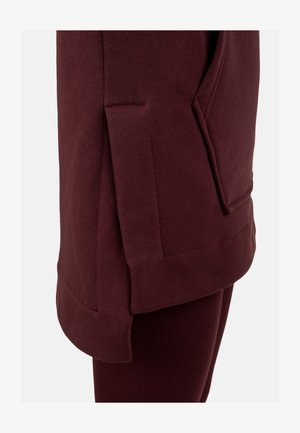 Sudadera burdeos con una abertura lateral y un gran bolsillo delantero. Material de algodón suave con una textura lisa y detalles cosidos.