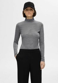 Grå langermet turtleneck topp, laget av teksturert materiale, kombinert med svarte vide bukser. Svart caps på hodet.