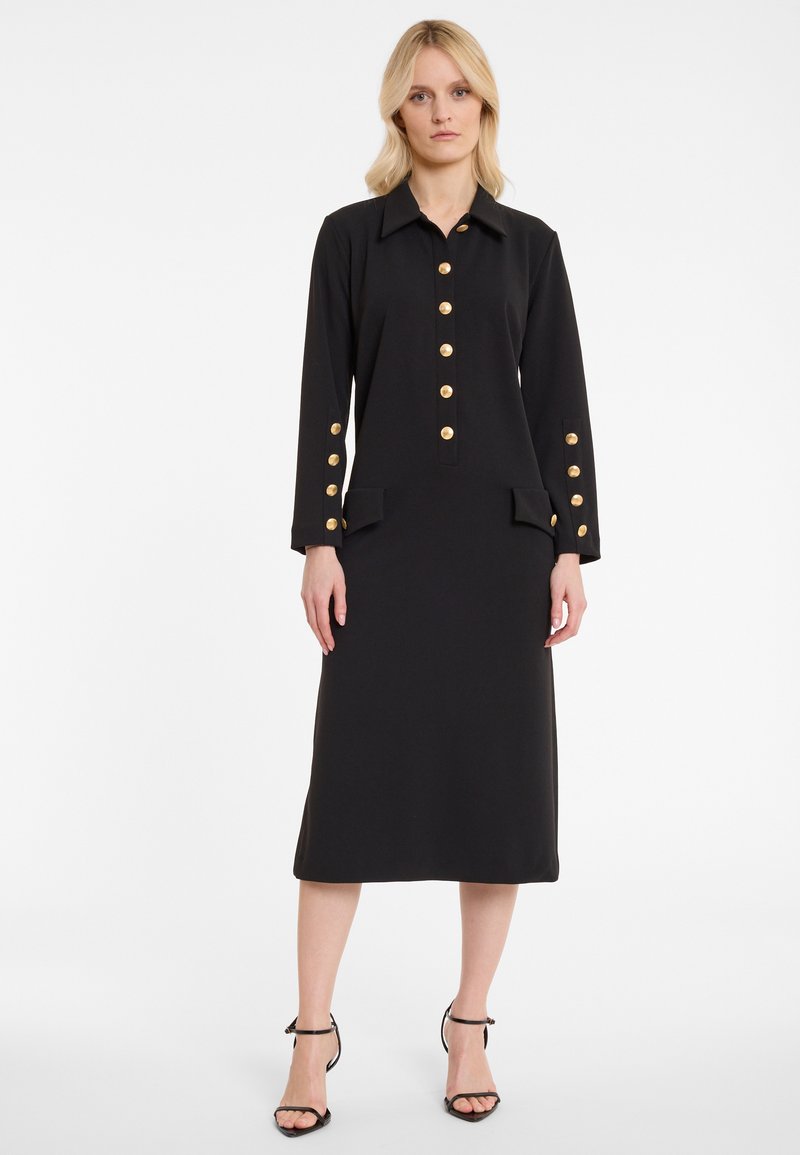 Schwarzes langärmeliges Kleid mit Kragen, goldener Knopfleiste und zwei vorderen Taschen. Glatte Stofftextur; knielange Länge.