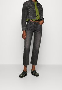 Cropped black denim jacket with front pockets, paired with a green crop top featuring black lettering, and high-waisted gray-striped jeans, accented by shiny clogs.