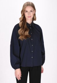 Camicia button-up blu navy con maniche a sbuffo, colletto classico e materiale di cotone morbido. Presenta sei bottoni frontali e una vestibilità rilassata.