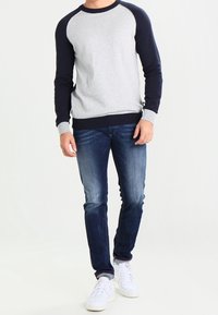 Grå och marinblå färgblockerad sweatshirt med rund hals, ribbad nederkant och mudd, ihopparad med mörkblå jeans och vita sneakers.