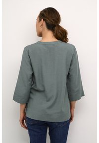 Camicia verde chiaro, morbida eamp; amp; amp;amp;... con maniche a tre quarti e scollo rotondo. Il tessuto appare testurizzato, con un design morbido e informale.