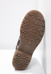 Semelle de chaussure noire avec un motif floral en relief. Présente une surface en caoutchouc texturée et une bande de roulement définie pour l'adhérence. Couleur marron avec une finition lisse.