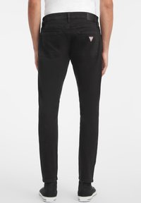 Sorte denimjeans med slim fit, fem lommer, med en liten triangel-logo på baklommen og en glatt tekstur.