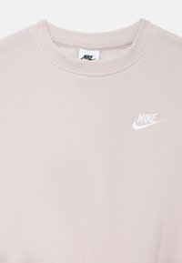 Svetloružová mikina Nike s okrúhlym výstrihom, rebrovanými manžetami a malým bielym logom na hrudi. Mäkká, hladká textúra látky.