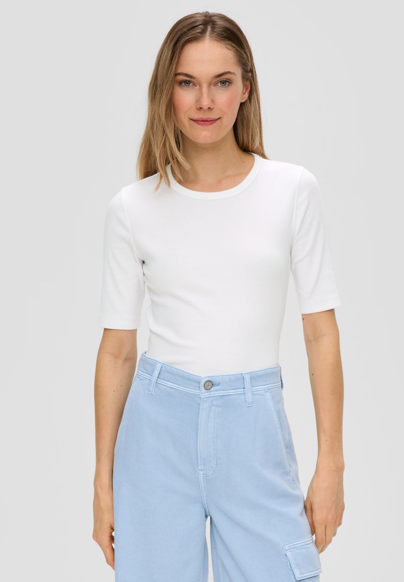 Weißes, eng anliegendes T-Shirt mit kurzen Ärmeln und rundem Halsausschnitt, kombiniert mit hellblauen, hoch taillierten Hosen mit Knopfverschluss und Taschen.