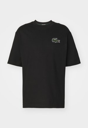 Zwart T-shirt met korte mouwen en ronde hals, met een klein groen krokodillenlogo op de linkerborst tegen een effen achtergrond.
