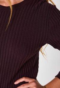 Maglione a coste di colore bordeaux scuro. Presenta un collo rotondo e maniche corte, mettendo in mostra un tessuto testurizzato con righe verticali.