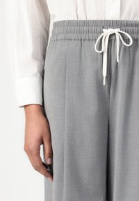 Grå tilpassede bukser med elastisk liv, hvit snor og glatt tekstur, supplert med en hvit skjorteutseende. 