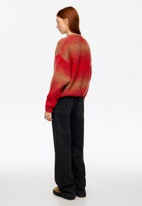 Sweter w cieniowaniu czerwieni i pomarańczy o luźnym kroju, wykonany z teksturowanego splotu, z długimi rękawami, zestawiony z czarnymi, szerokimi spodniami z wysokim stanem i butami.