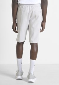 Shorts de sport gris clair avec une taille élastique, deux poches arrière et un design épuré, associés à des chaussettes blanches et des baskets grises.