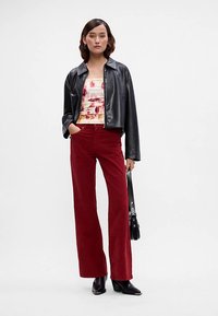 Melnā nolocītā ādas jaciņa, krāsaina tie-dye topiņa ar rozā un dzeltenu nokrāsu, sarkanas kordurojas svārku bikses un melni potītes zābaki, kopā ar melnu plecu somu.