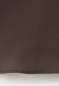 Gros plan sur un tissu lisse de couleur brun foncé avec une texture fine et un ourlet cousu le long du bord inférieur, sur un fond gris clair.