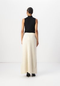 Black sleeveless top paired with a long, textured cream skirt. Skirt features a soft, fluffy fabric and a fitted waist. Black boots complete the look.