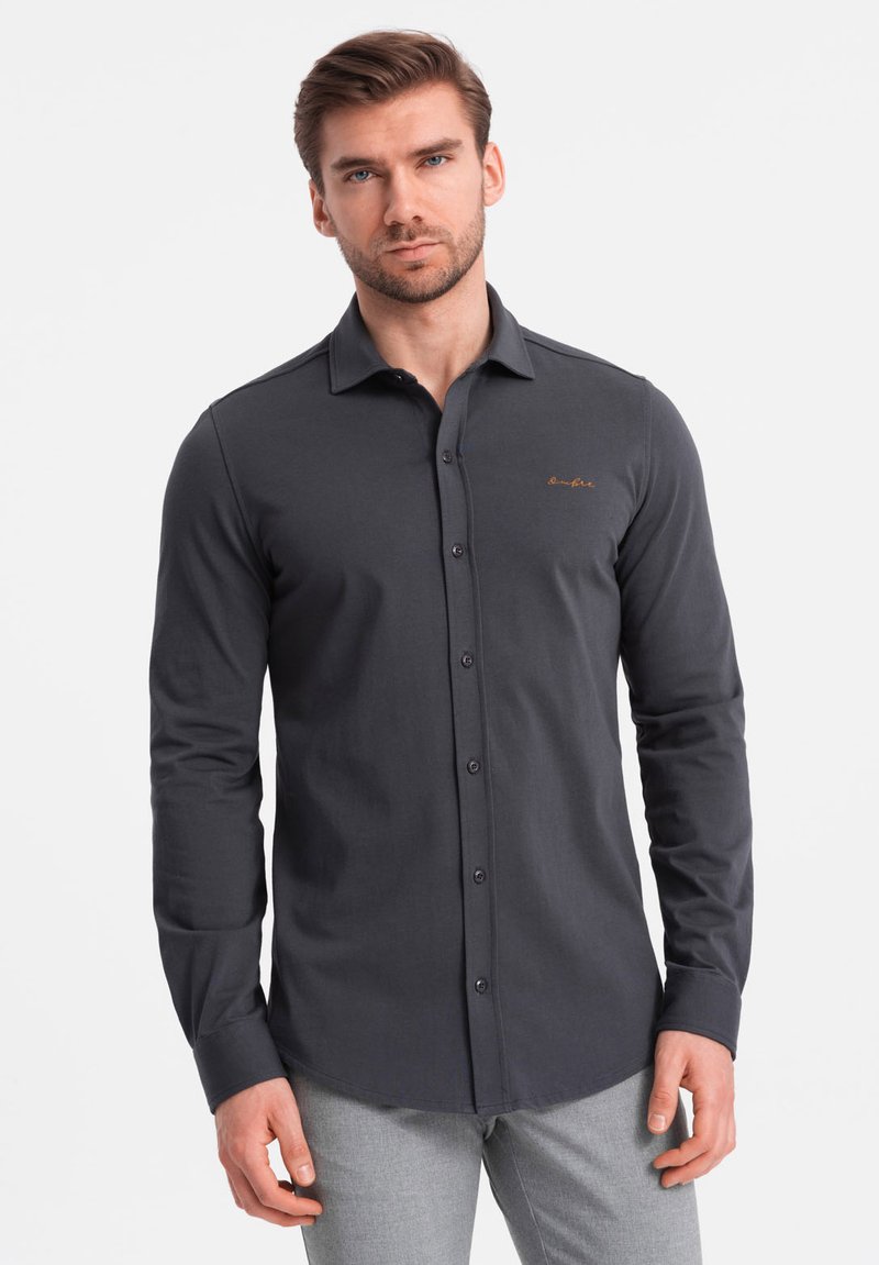 Donkergrijze langarmshirt met een knoopsluiting aan de voorkant, een scherpe kraag en een geborduurd logo op de borst. De stof lijkt glad en aansluitend.
