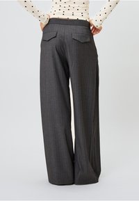 Pelēki svītraini platā griezuma bikses ar plakanu jostu un divām aizmugurējām kabatām, demonstrējot gludu tekstūru un pielāgotu piegriezumu.