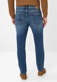 Jeans in denim blu con una vestibilità slim, dotati di due tasche posteriori, cuciture a contrasto e un'etichetta in pelle marrone sulla cintura.