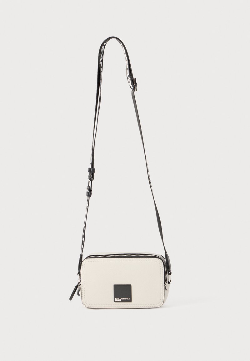 Rectangular crossbody bag in light gray material, featuring a black zip, logo plaque, and adjustable strap with a patterned accent.