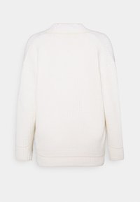 Bílý texturovaný svetr s žebrovaným designem a kulatým výstřihem. Má spadlá ramena a volný střih. Švy podél okrajů.