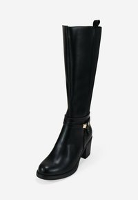 Bota de cuero negra hasta la rodilla con tacón cuadrado, panel elástico lateral y correa decorativa con hebilla metálica alrededor del tobillo.