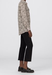Camicia beige a maniche lunghe con motivo a foglie nere, abbinata a jeans neri a vita alta e mocassini neri con suola spessa e dettagli dorati.