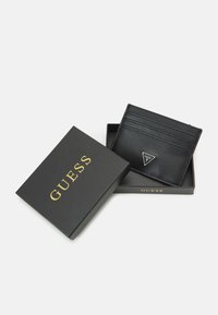 Cardholder din piele neagră, cu multiple sloturi și un logo triunghiular. Vine într-o cutie neagră cu "GUESS" imprimat în aur.