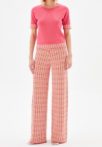 Rosa stickad topp med korta ärmar och rutiga vida byxor i mönster av röd, gul och kräm, med kontrasterande detaljer och mjuk textur.