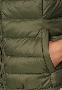 Olivově zelená péřová bunda s horizontálním prošíváním, obsahující boční kapsu a hladký, lesklý povrch látky. Zip na přední straně.