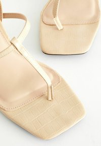 Beige sandály na vyšším podpatku se čtveratou špičkou, textura umělé kůže se vzorem krokodýla a minimalistickým designem popruhů.