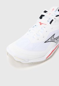 Fehér sportcipő texturált hálós felsőrésszel, fekete és piros részletekkel, párnázott talppal. Hagyományos fűzőkkel.