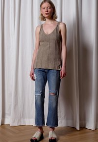 Top de malha castanho claro com decote em V, combinado com jeans azuis desgastados e chinelos bege de abertura na frente. Design simples e moderno.