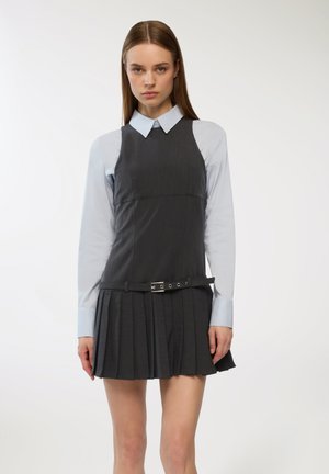 Abito grigio a pieghe con corpino aderente, sovrapposto a una camicia colletto azzurro. Presenta una cintura con dettaglio della fibbia in argento.