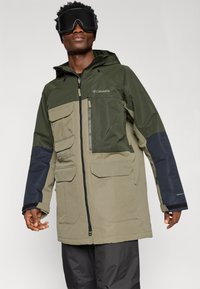 Žalias ir chaki spalvos vandeniui atsparus džemperis su keliais kišeniais, užtrauktuku priekyje ir reguliuojama kepure. Savybės: juodi akcentai ant rankovių.